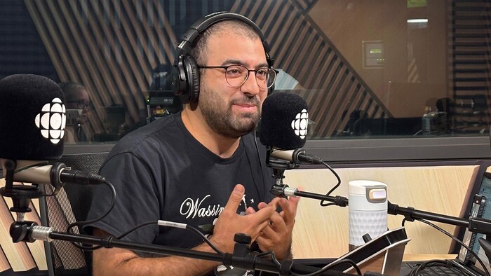 Un homme souriant devant un micro dans un studio de radio.
