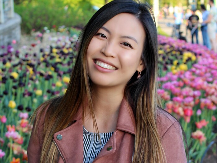 Jenn Taing pose, souriante, devant un parterre de tulipes colorées.