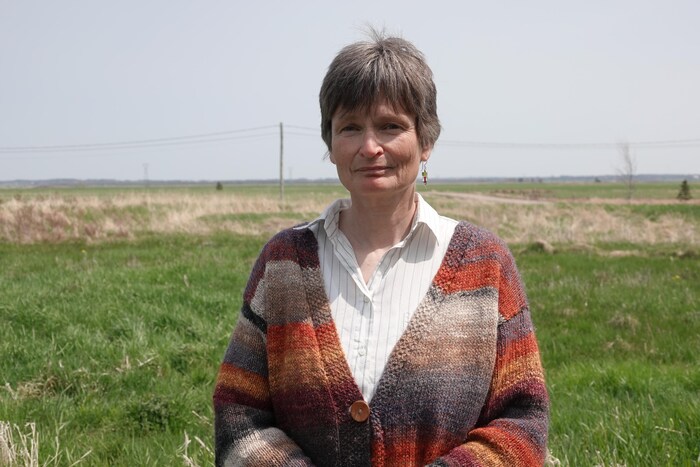Sabine Dietz est debout devant une grande étendue de terrain plat où pousse de l'herbe.