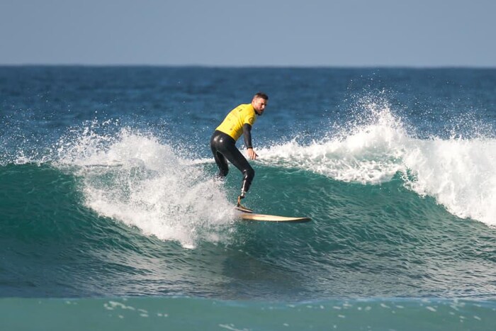 Muni d'une prothèse à la jambe droite, un homme file sur une vague sur son surf. 