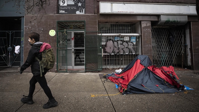 Un passant marche devant une tente dans le quartier Downtown Eastside, à Vancouver.