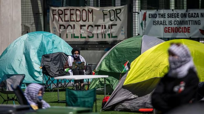 Des tentes, des chaises et des tables sont installées sur un terrain de gazon artificiel avec des banderoles en support de la Palestine.  