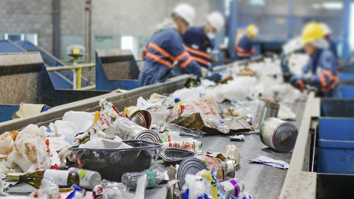 Des déchets mixtes de métal, de plastique et de papier sur un tapis roulant dans un centre de recyclage sont triés par des employés.