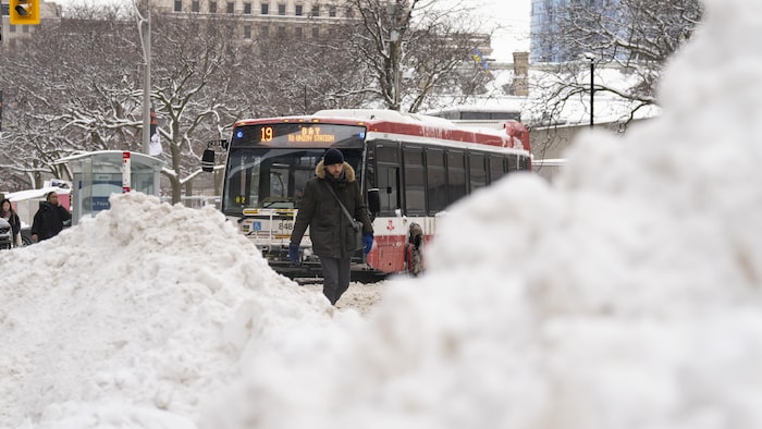 Des passants marchent dans une rue très enneigée où un autobus circule.