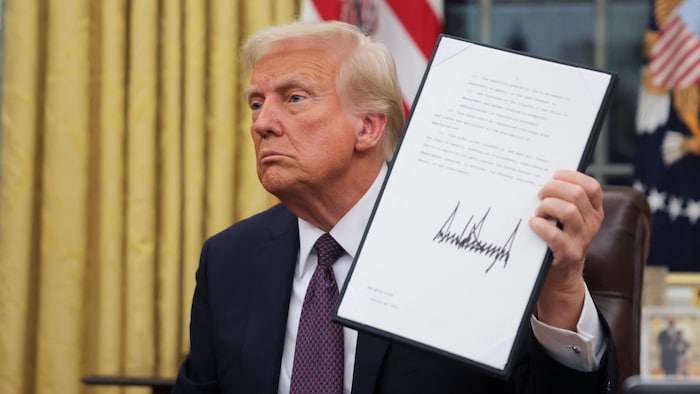 Donald Trump, dans le bureau ovale, exhibe un des documents qu'il a signés.