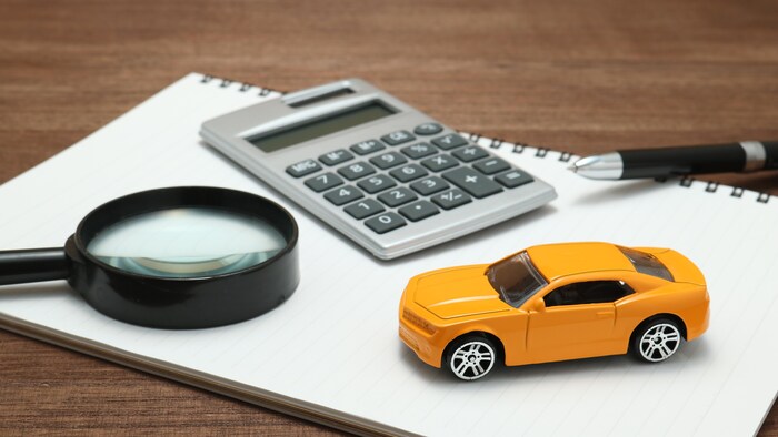 Une voiture miniature, un cahier, un stylo et une loupe sur un bureau.
