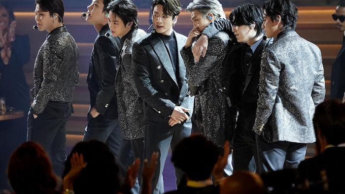 Les 7 membres de BTS se tiennent en rangée et posent de différentes façons. Ils portent des vestons, dont certains des vestons avec des brillants. Chacun d'eux a un micro casque et semble en train de chanter.