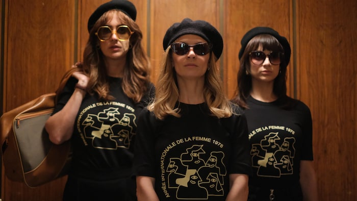 Trois femmes portent un béret et un t-shirt sur lequel est inscrit Année internationale de la femme 1975.