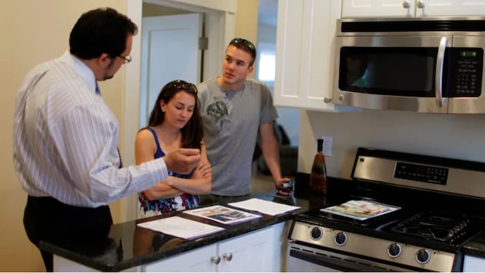 Image d'intérieur : un courtier immobilier montre les documents liés à une maison à vendre à de jeunes acheteurs.