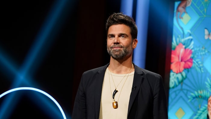 Un homme porte une veste noire et des bijoux.
