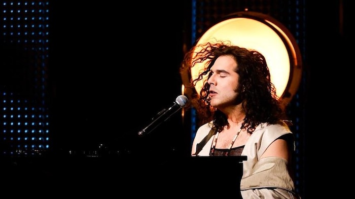 Le chanteur est installé derrière son piano et chante les yeux fermés.