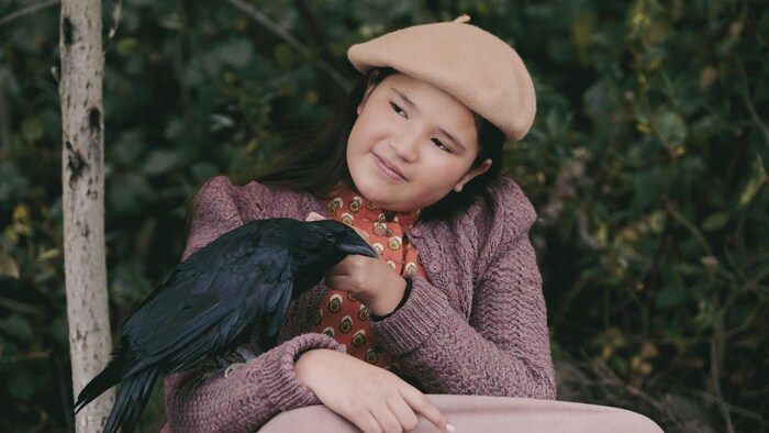 Une jeune fille portant un béret tient un corbeau sur son bras.