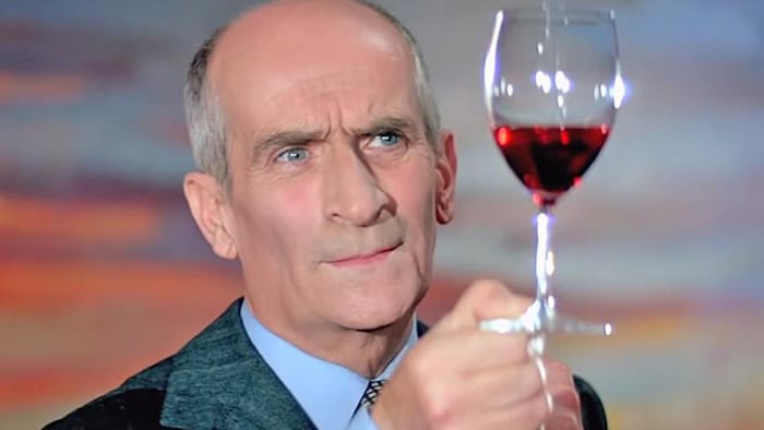 Un homme regarde un verre de vin rouge qu'il tient au bout de ses doigts.