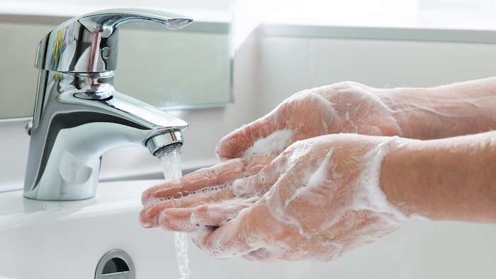 Gros plan sur des mains qui sont pleines de savon sous un robinet.