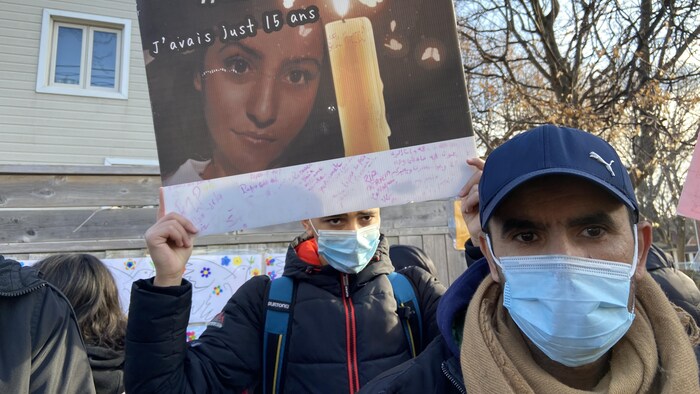 Un homme avec un masque à côté d'un adolescent portant une pancarte.