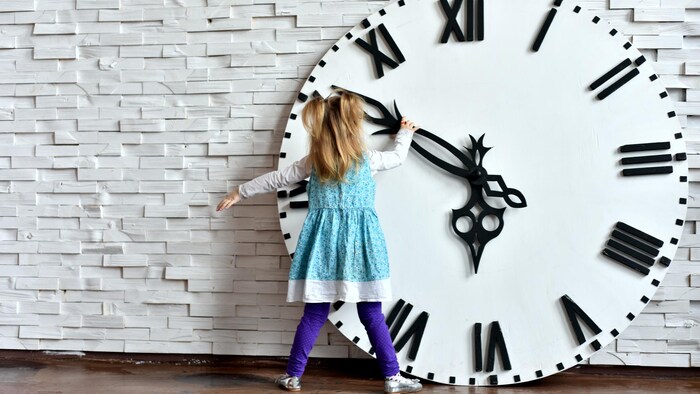Une petite fille fait tourner l'aiguille d'une horloge surdimensionnée. 