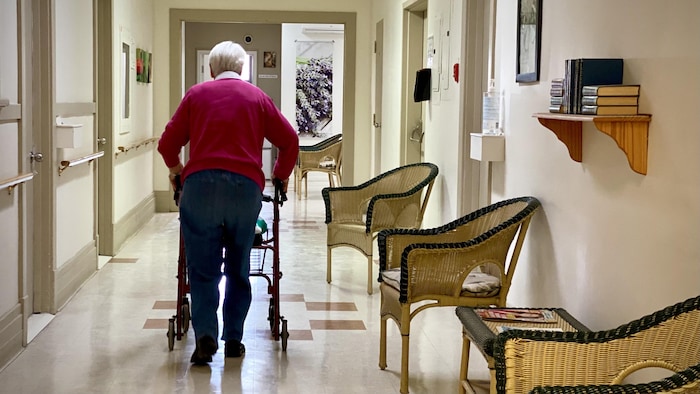Une personne âgée se déplace avec une marchette dans le corridor d'une résidence privée pour aînés.
