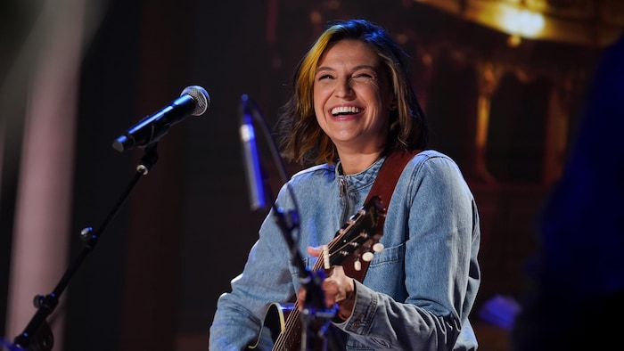 Sara Dufour sourit devant un micro, guitare à la main.