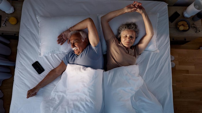 Deux personnages âgées sont couchées dans un lit double.