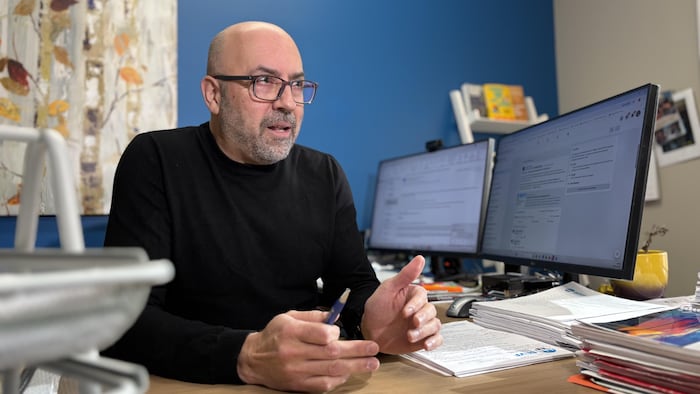 Un homme est assis derrière un bureau, près d’un ordinateur.