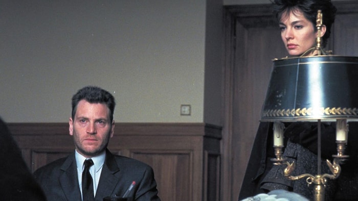 Tchéky Karyo est assis, Anne Parillaud est debout, tous deux devant un bureau.