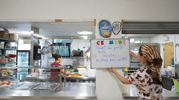 L'une des cuisinières est en train d'accrocher le menu du midi au mur.