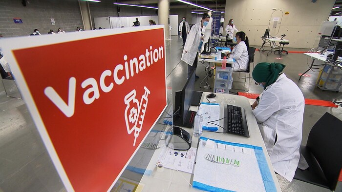 Pancarte avec le mot vaccination inscrit dessus dans un local avec du personnel de la santé.