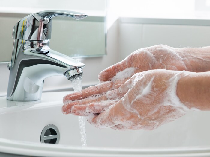Gros plan sur des mains qui sont pleines de savon sous un robinet.