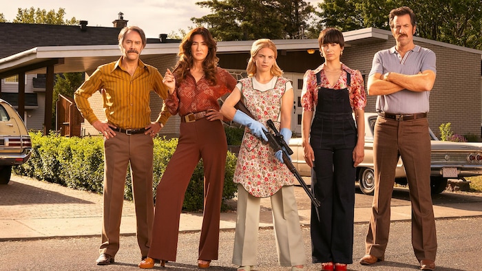 Cinq personnages de la série posent dans la rue, la femme au milieu tenant une carabine.