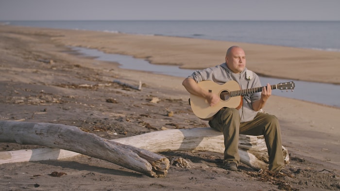 Un homme sur le bord de la plage avec sa guitare.