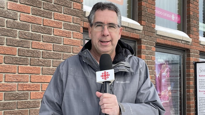 Francis Bouchard se tient debout avec un micro devant un mur de briques.
