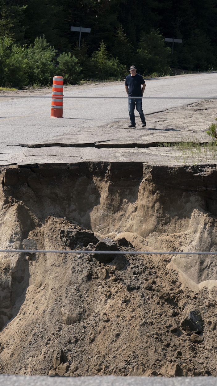 Un homme marche vers le bord d'une grosse crevasse au beau milieu d'une route.