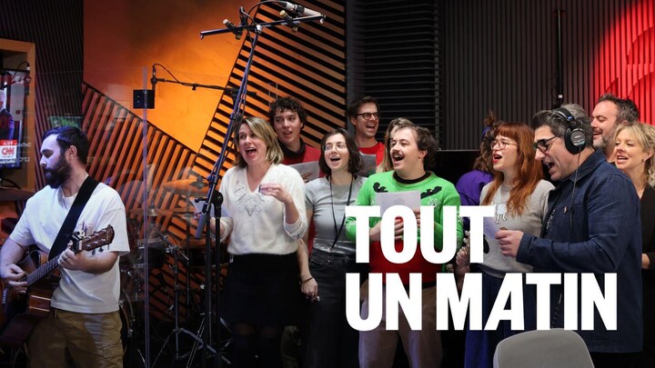 Plusieurs personnes chantent derrière un micro, et une autre personne est à la guitare. 
