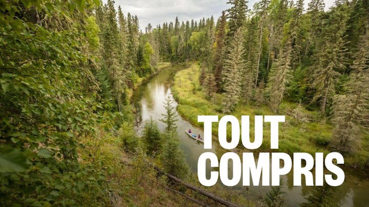 Deux personnes avancent en canot sur une rivière entourée d'une forêt dense.