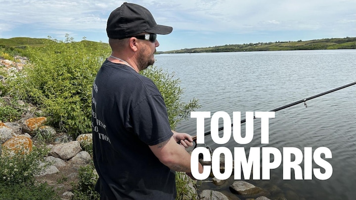 Un homme tient une canne à pêche dans ses mains, il est au bord d'une rivière.