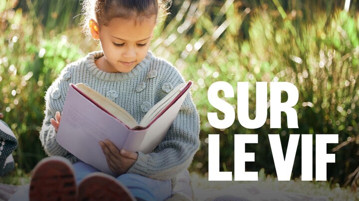 Une jeune fille en train de lire un grand livre à l'extérieur.