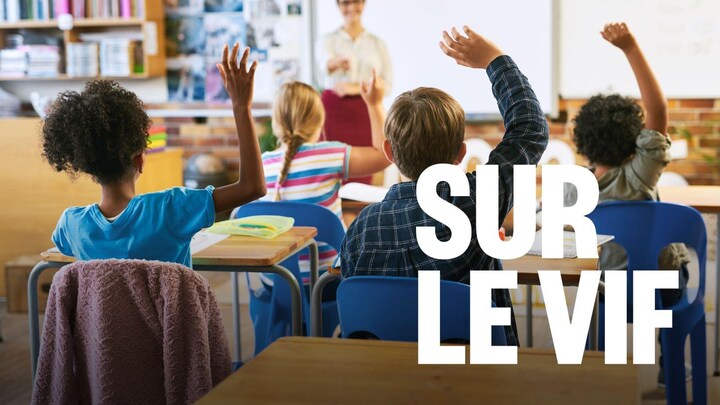 Des élèves dans une classe d'école. Ils ont une main   levée dans les airs.