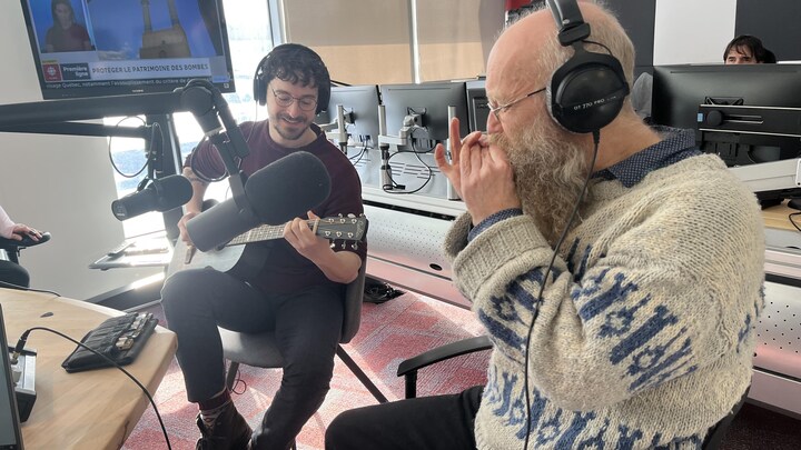 un jeune homme guitariste et un homme plus âgé à l'harmonica jouent de leurs instruments dans un studio radio