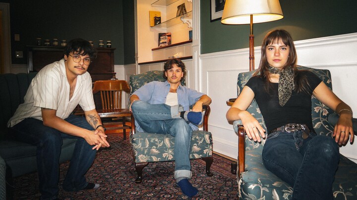 Les trois membres du groupe sont assis chacun dans un fauteuil lors d'une séance photo.
