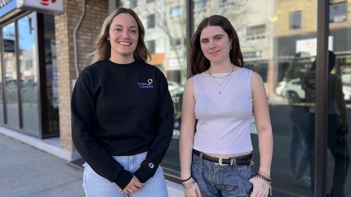 Deux femmes debout côte à côte à l'extérieur sourient à la caméra.