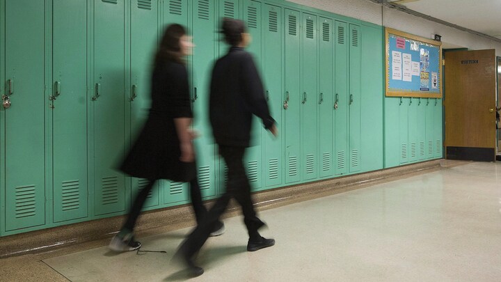 Des élèves marchent devant des casiers dans un corridor d'école.