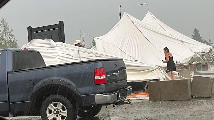 La photo, prise de l'intérieur d'un véhicule, montre que pendant la pluie battante, une femme et un homme se tiennent près du chapiteau effondré et discutent. 