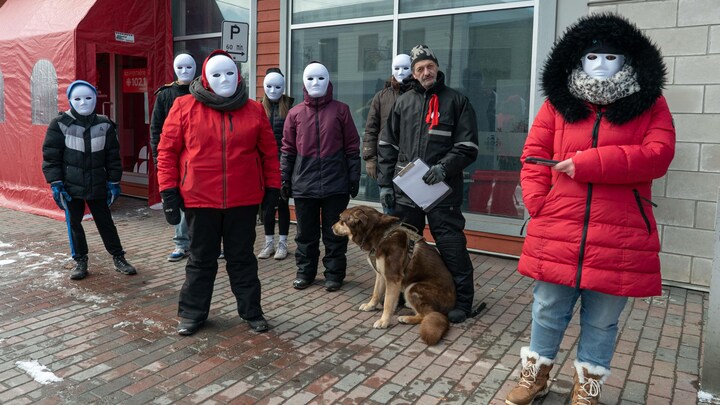 Des manifestants masqués sont debout sur le trottoir.