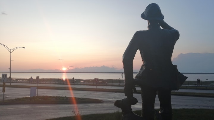 Une statue représentant un homme et son chien qui regardent au loin devant le coucher de soleil.