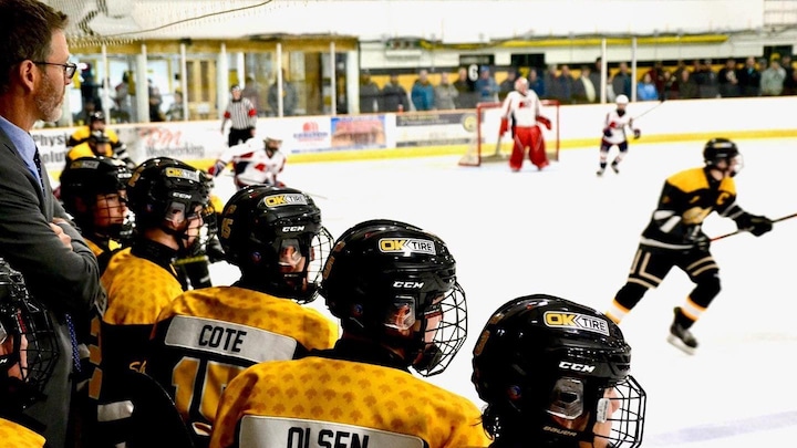 Des joueurs de hockey assis au banc regardent un match.