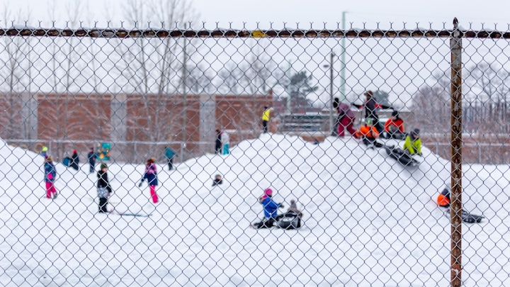 Des enfants de niveau primaire qui jouent sur une butte de neige dans un cour d'école.