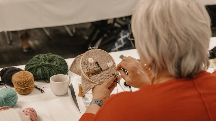 Une dame de dos passe un fil à travers un projet de broderie en laine.