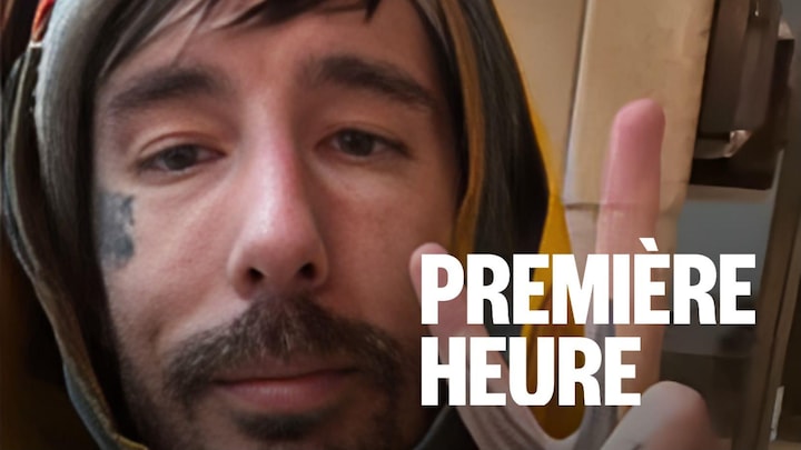 Un homme regarde la caméra en faisant un signe de la main de salut.
