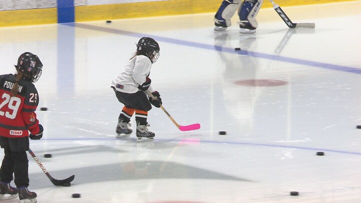 Une jeune fille apprend à jouer au hockey sur une patinoire.