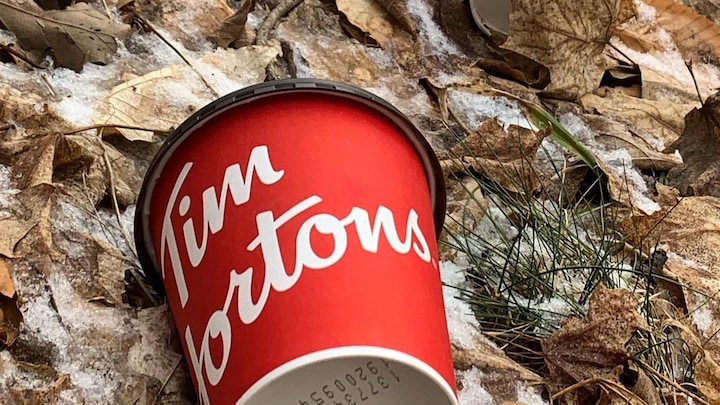 Tasse en papier de la compagnie canadienne Tim Hortons sur le sol dans un espace naturel.